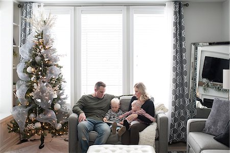 Young family sitting on sofa, looking at book Stock Photo - Premium Royalty-Free, Code: 614-08881362