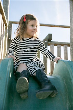 Cute girl in striped dress sitting on playground slide Stock Photo - Premium Royalty-Free, Code: 614-08908276