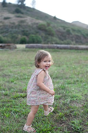 Cute female toddler running in field looking over her shoulder Stock Photo - Premium Royalty-Free, Code: 614-08908312