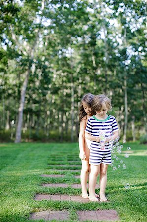 Girl and boy watching bubbles from toy bubble maker in garden Stock Photo - Premium Royalty-Free, Code: 614-08908409