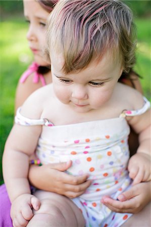 Close up of female toddler sitting on girl's knee in garden Stock Photo - Premium Royalty-Free, Code: 614-08908423