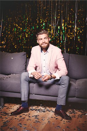 Man sitting on sofa at party, glitter covering floor Stock Photo - Premium Royalty-Free, Code: 614-08983355