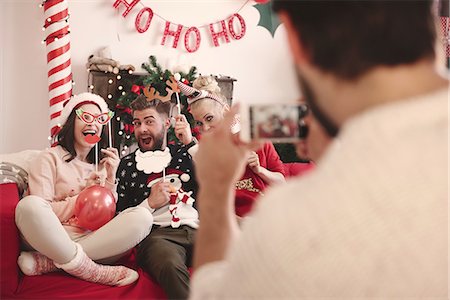 simsearch:693-06435898,k - Over shoulder view of young man photographing friends on sofa at christmas party Stock Photo - Premium Royalty-Free, Code: 614-08983466