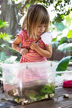 Girl looking into fishing net from plastic tadpole pond on garden table Stock Photo - Premium Royalty-Free, Code: 614-08990591