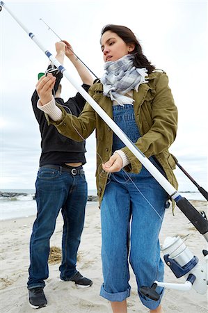 Young couple preparing sea fishing rods on beach Stock Photo - Premium Royalty-Free, Code: 614-08990776