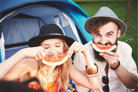 Young couple in trilbies making smiley face with melon slice at festival Stock Photo - Premium Royalty-Free, Code: 614-08991280