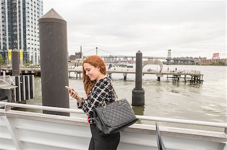 Young businesswoman on ferry deck looking at smartphone, New York, USA Stock Photo - Premium Royalty-Free, Code: 614-09017552