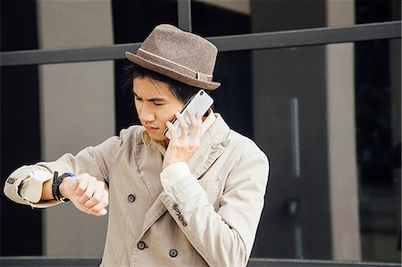 pantsuit - Young man outdoors, using smartphone, looking at wristwatch Stock Photo - Premium Royalty-Free, Code: 614-09018004