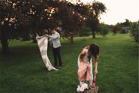 Young couple preparing picnic blanket and pink champagne in park at dusk Stock Photo - Premium Royalty-Free, Code: 614-09026484