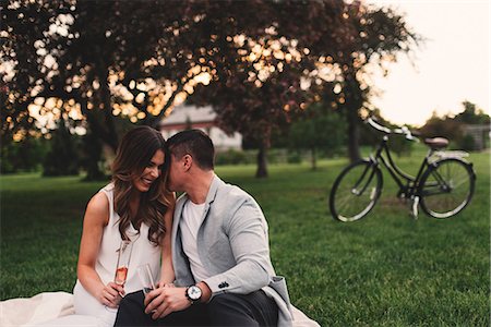 Romantic young couple with pink champagne whispering in park at dusk Stock Photo - Premium Royalty-Free, Code: 614-09026488