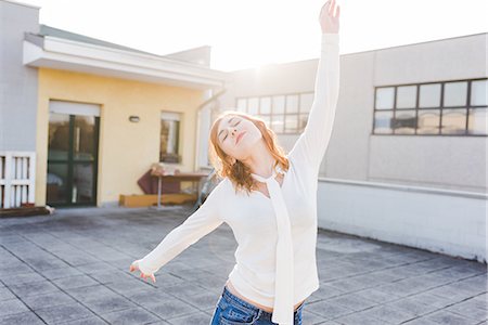 simsearch:614-09078761,k - Beautiful young woman dancing on sunlit roof terrace with eyes closed Stock Photo - Premium Royalty-Free, Code: 614-09026685