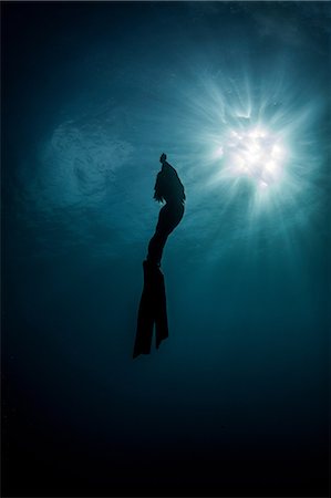 Underwater view of silhouetted female free diver moving up towards sun rays,  New Providence, Bahamas Stock Photo - Premium Royalty-Free, Code: 614-09027049