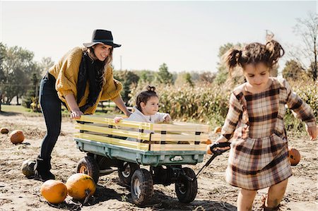 Mother and daughters playing together in pumpkin patch, young girl being pulled along in cart Stock Photo - Premium Royalty-Free, Code: 614-09079154