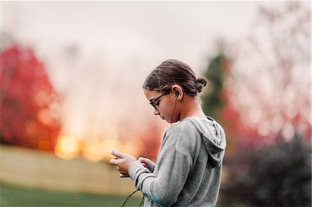 Side view of girl listening to earphone music looking at smartphone in garden Stock Photo - Premium Royalty-Free, Code: 614-09079158