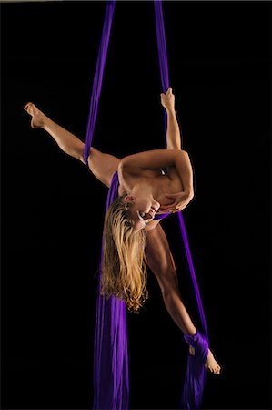 Nude young female aerial acrobat hanging upside down with torso wrapped in silk rope against black background Foto de stock - Sin royalties Premium, Código: 614-09110719