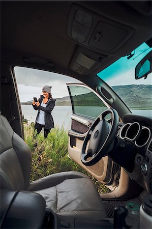 simsearch:614-09078761,k - Young woman standing beside Dillon Reservoir, holding smartphone, view through parked car, Silverthorne, Colorado, USA Stock Photo - Premium Royalty-Free, Code: 614-09127167