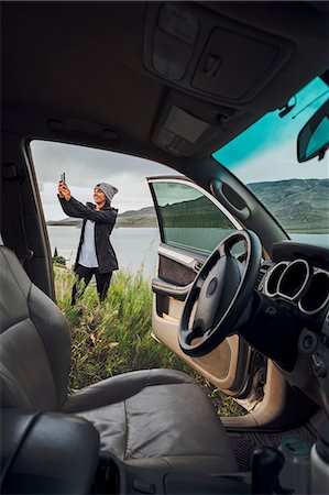 simsearch:614-09078761,k - Young woman standing beside Dillon Reservoir, holding smartphone, view through parked car, Silverthorne, Colorado, USA Stock Photo - Premium Royalty-Free, Code: 614-09127169