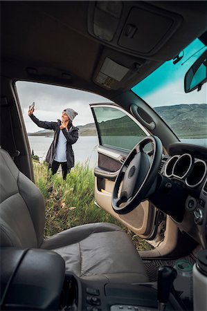 simsearch:614-09078761,k - Young woman standing beside Dillon Reservoir, holding smartphone, view through parked car, Silverthorne, Colorado, USA Stock Photo - Premium Royalty-Free, Code: 614-09127170