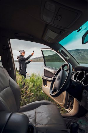 simsearch:614-09078761,k - Young woman standing beside Dillon Reservoir, holding smartphone, view through parked car, Silverthorne, Colorado, USA Stock Photo - Premium Royalty-Free, Code: 614-09127171