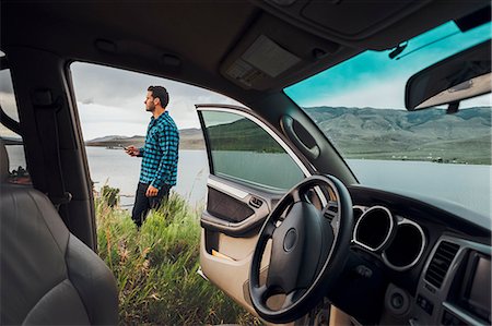 full body cell - Mid adult man standing beside Dillon Reservoir, holding smartphone, view through parked car, Silverthorne, Colorado, USA Stock Photo - Premium Royalty-Free, Code: 614-09127237