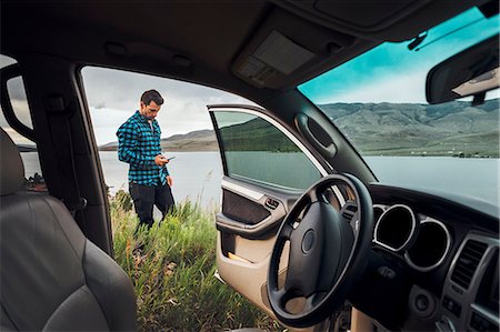 Mid adult man standing beside Dillon Reservoir, holding smartphone, view through parked car, Silverthorne, Colorado, USA Stock Photo - Premium Royalty-Free, Code: 614-09127238