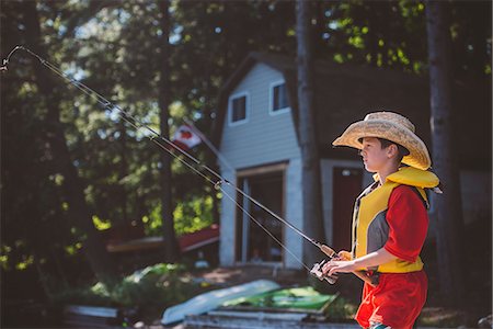 Boy in cowboy hat fishing from lakeside Stock Photo - Premium Royalty-Free, Code: 614-09127291