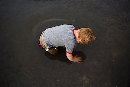Boy kneeling in puddle on road Stock Photo - Premium Royalty-Free, Code: 614-09168221