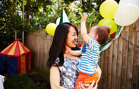 Mother wearing party hat holding baby boy at birthday party Stock Photo - Premium Royalty-Free, Code: 614-09210444