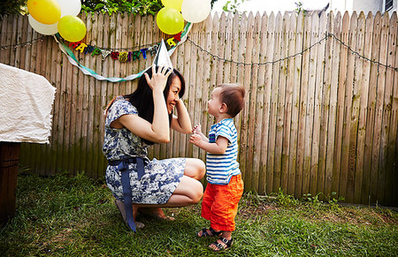 Mother crouching down putting on party hat Stock Photo - Premium Royalty-Free, Code: 614-09210445