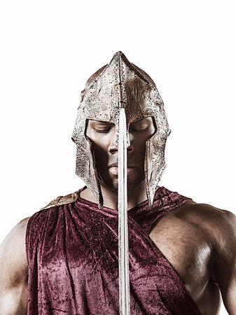 Studio portrait of poised young man dressed as gladiator with helmet and sword Stock Photo - Premium Royalty-Free, Code: 614-09211284