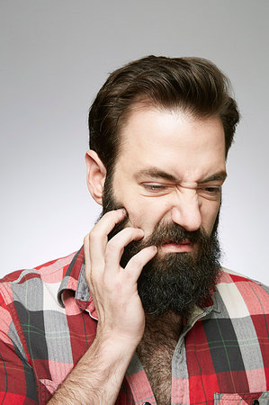 people itch scratch - Studio portrait of young man scratching overgrown beard Photographie de stock - Premium Libres de Droits, Code: 614-09211511