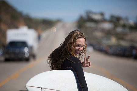simsearch:614-06896253,k - Rear view of young woman carrying surfboard looking over shoulder, sticking tongue out, doing peace sign Stock Photo - Premium Royalty-Free, Code: 614-09212308