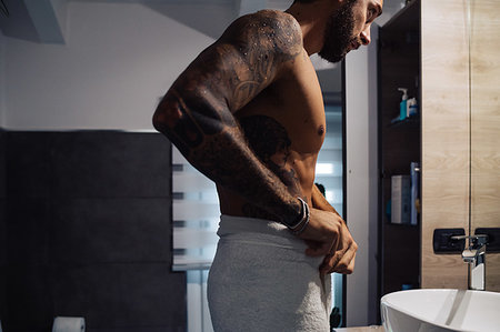 simsearch:614-03982063,k - Mid adult man with tattoos putting towel around waist at bathroom mirror Photographie de stock - Premium Libres de Droits, Code: 614-09258514