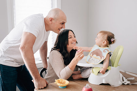 simsearch:614-06896477,k - Mother and father feeding baby daughter in child seat on kitchen table Stock Photo - Premium Royalty-Free, Code: 614-09258596