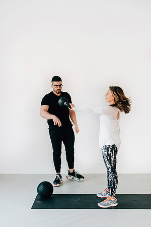 female wearing trainers - Fitness instructor observing woman lifting kettlebell in studio Stock Photo - Premium Royalty-Free, Code: 614-09276242