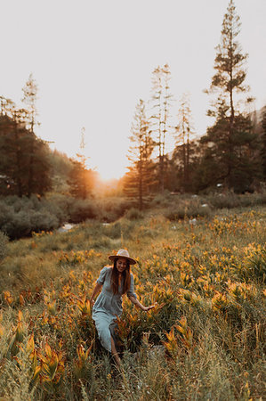 simsearch:614-09078761,k - Young woman in maxi dress and stetson walking through wildflowers at sunset in rural valley, Mineral King, California, USA Stock Photo - Premium Royalty-Free, Code: 614-09270486
