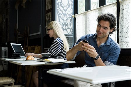 Man with cellphone and woman with laptop in cafe Stock Photo - Premium Royalty-Free, Code: 614-03649620