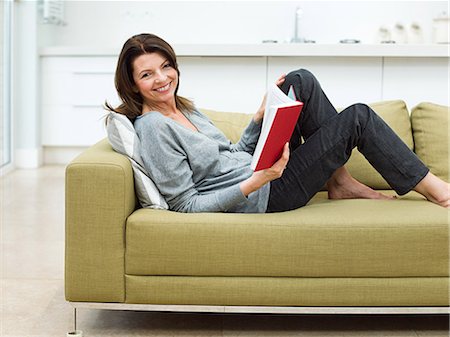 Mature woman sitting on sofa reading book Stock Photo - Premium Royalty-Free, Code: 614-03763774