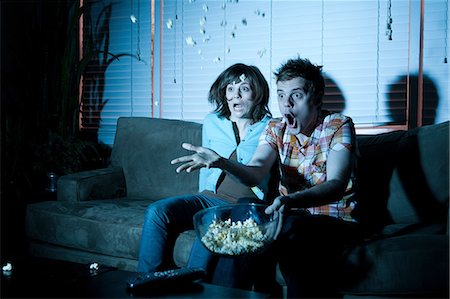 film movies - Young couple watching tv, man throwing popcorn Stock Photo - Premium Royalty-Free, Code: 614-03981536