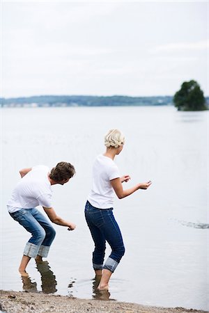A man and a woman throwing pebbles trying to make them bounce on the surface of the water, Sweden. Stock Photo - Premium Royalty-Free, Code: 6102-03866836