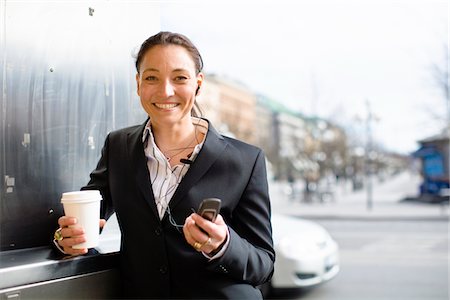simsearch:6102-07455789,k - Portrait of cheerful businesswoman with takeaway coffee in one hand and mobile phone in another Stock Photo - Premium Royalty-Free, Code: 6102-04929592
