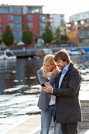 Couple standing on promenade using cell phone together Stock Photo - Premium Royalty-Free, Code: 6102-06777359