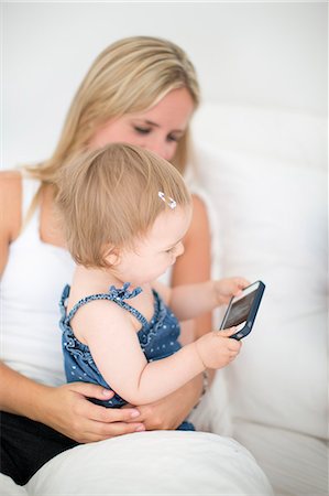 Little girl sitting on mothers lap and holding cell phone Photographie de stock - Premium Libres de Droits, Code: 6102-06965512