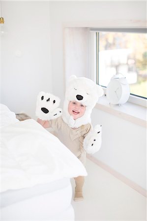 Girl wearing polar bear costume hiding behind bed Stock Photo - Premium Royalty-Free, Code: 6102-07842731