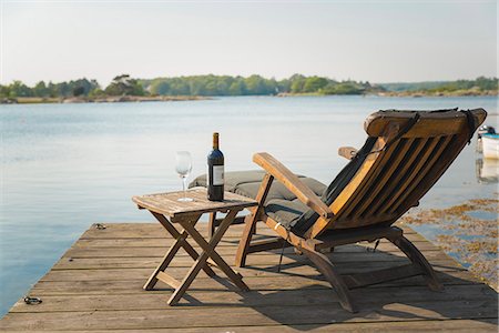 Lounge chair and wine bottle on table on jetty Stock Photo - Premium Royalty-Free, Code: 6102-07843744