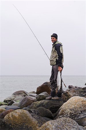 simsearch:6102-08001381,k - Smiling man standing on coastline and holding fishing rod and fish Stock Photo - Premium Royalty-Free, Code: 6102-08558898
