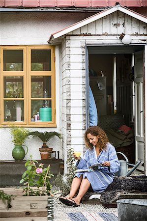 Woman reading magazine in front of house Photographie de stock - Premium Libres de Droits, Code: 6102-08521003