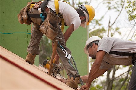 simsearch:6105-06043034,k - Carpenters with safety harness using circular saw to trim skylight opening in roof Stock Photo - Premium Royalty-Free, Code: 6105-05396297