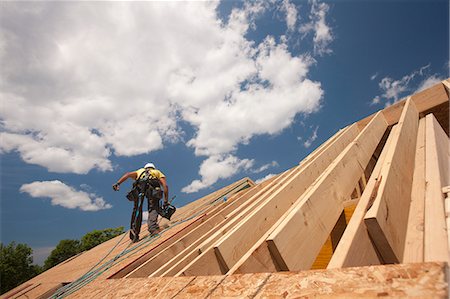 Carpenter holding a nail gun on the roof of a house under construction Stock Photo - Premium Royalty-Free, Code: 6105-05396232