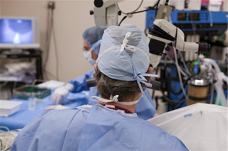 photos of us doctors - Doctor looking in microscope during surgery with surgical technician taking next instrument Stock Photo - Premium Royalty-Free, Code: 6105-05396731